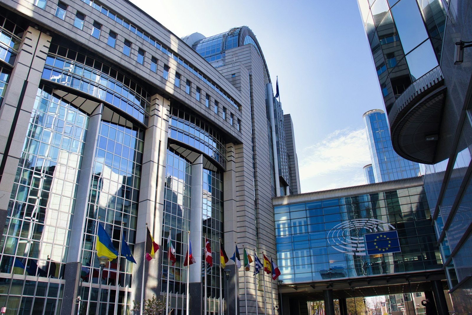 Le bâtiment du Parlement européen à Bruxelles, façade vitrée moderne sous un ciel bleu, drapeaux au premier plan.